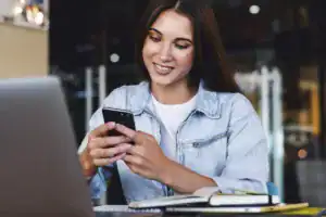 Jovem sorridente usando o smartphone na mesa de trabalho, ilustrando a agilidade e a praticidade da IA para atendimento no WhatsApp.