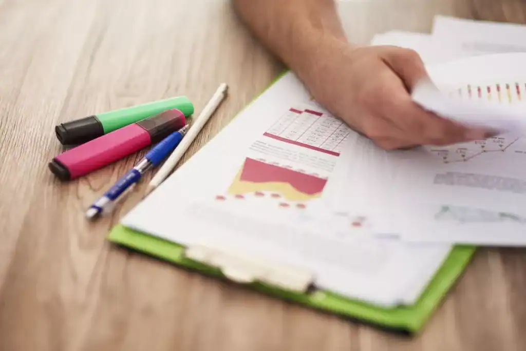 Resultados da pesquisa de satisfação escolar ilustrados em gráficos impressos sendo analisados por uma pessoa segurando papéis sobre uma prancheta.