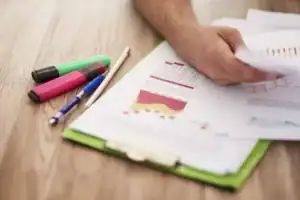 Resultados da pesquisa de satisfação escolar ilustrados em gráficos impressos sendo analisados por uma pessoa segurando papéis sobre uma prancheta.